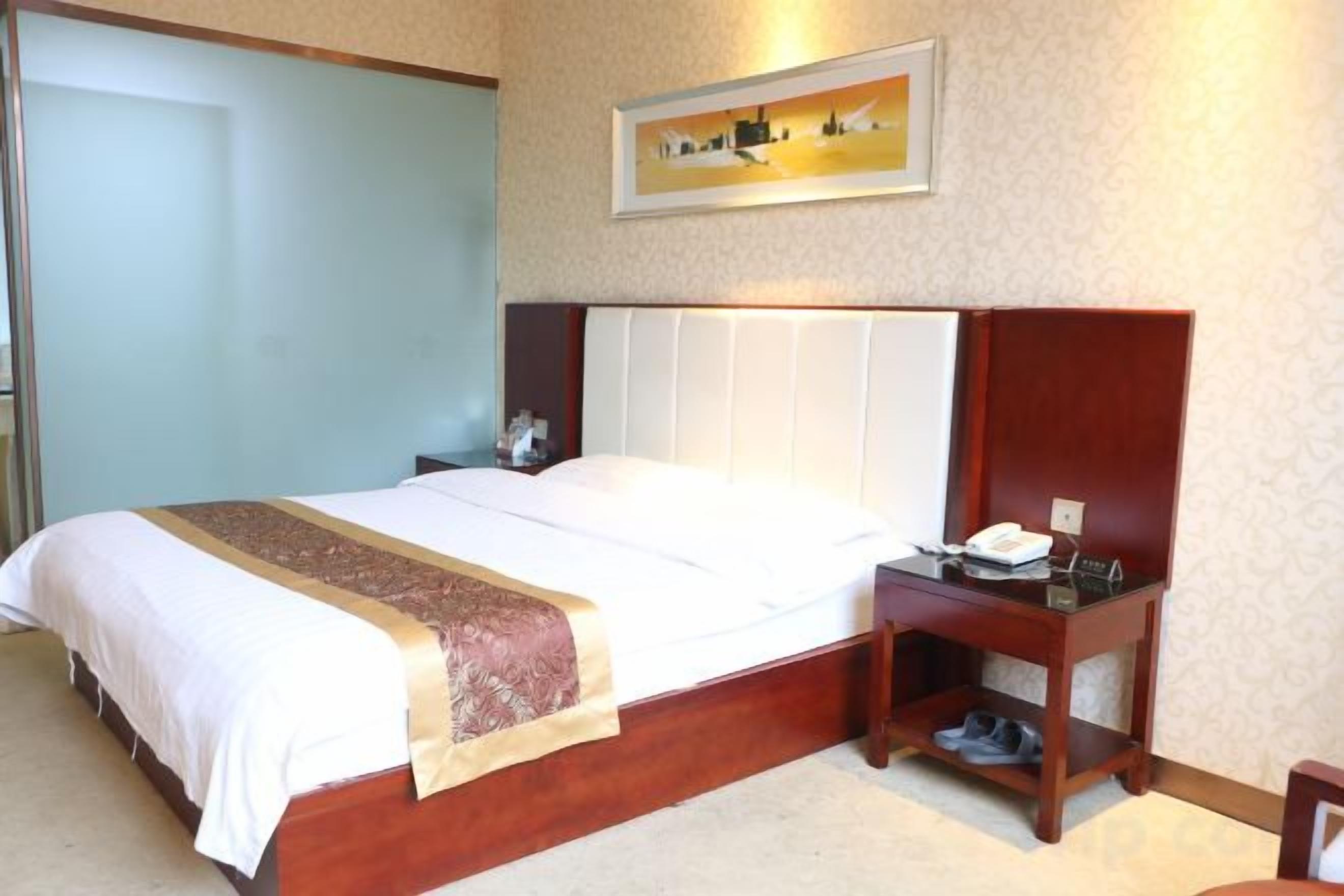Una habitación de hotel con una cama, una mesita de noche y un escritorio pequeño con un teléfono.