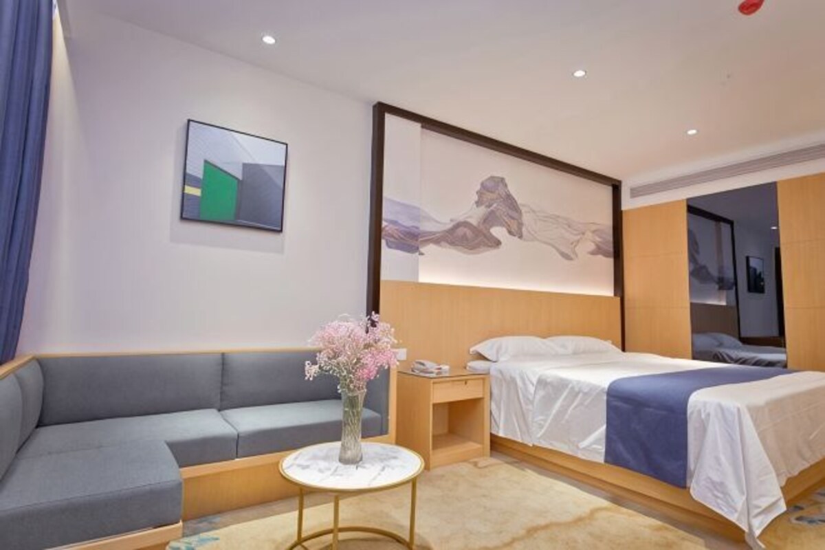 A hotel room with a sofa, a bed, a small table with a vase, and artwork on the walls.