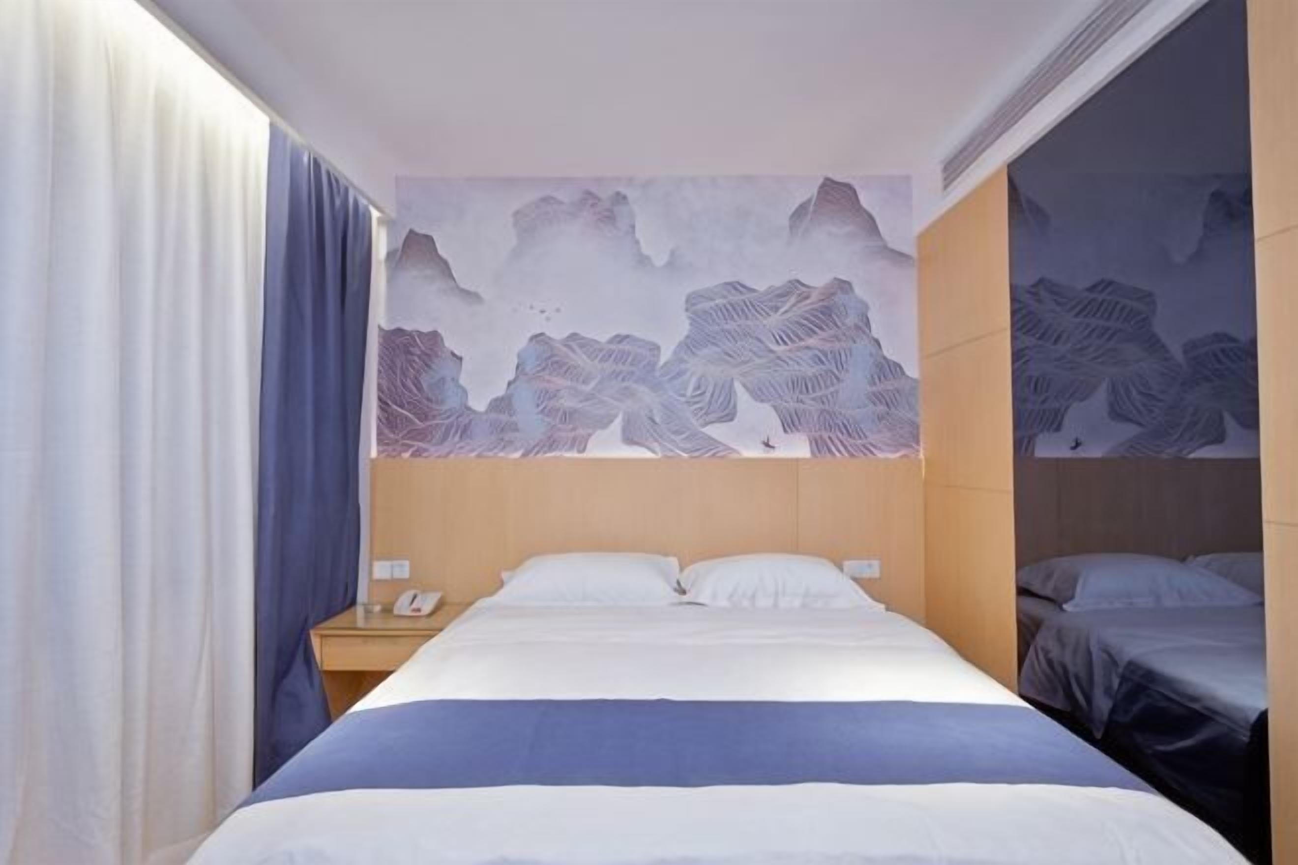 A hotel room with a large bed, a nightstand, a wall-mounted telephone, and a window with curtains.