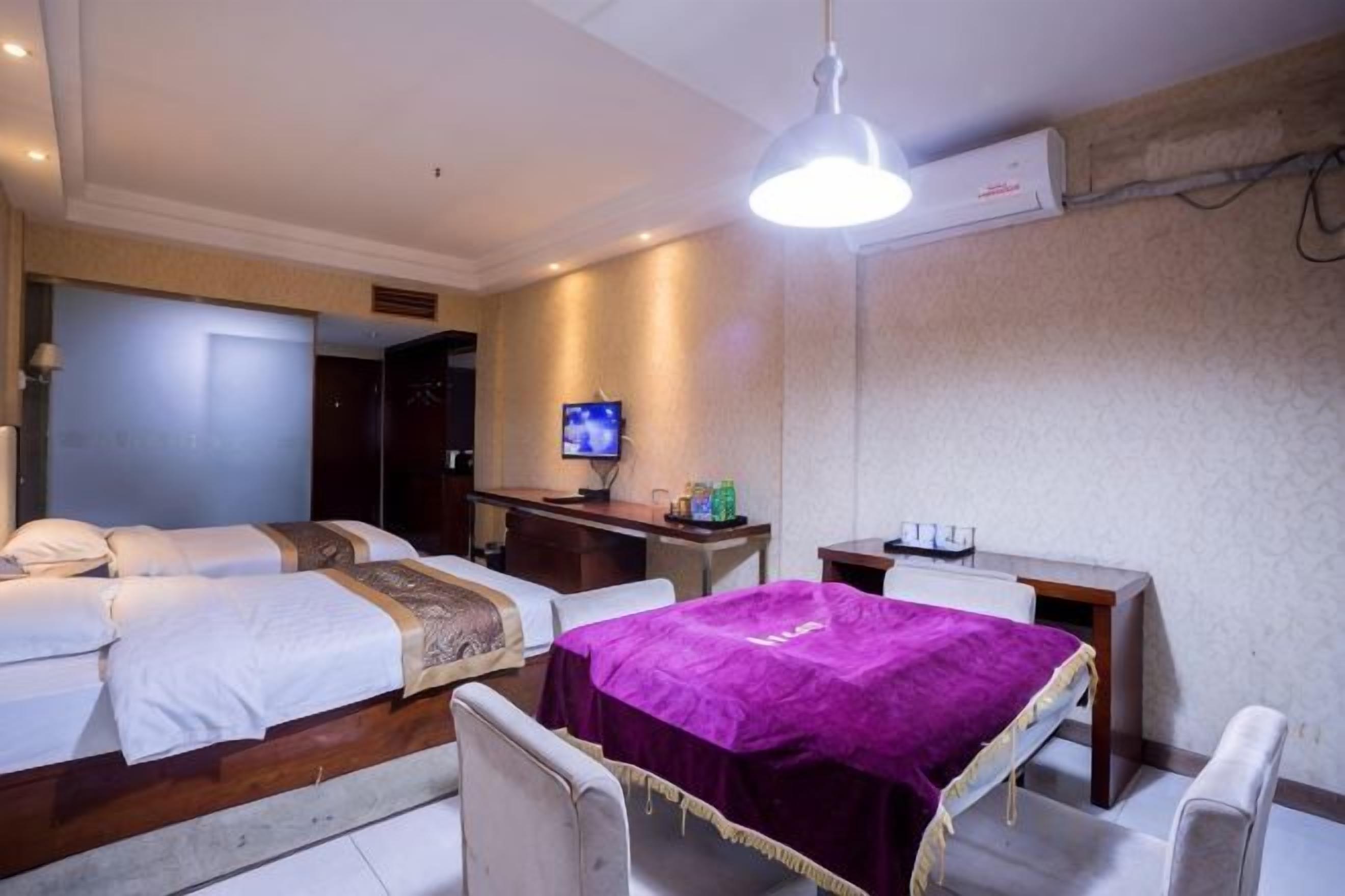 A hotel room with two beds, a desk, a chair, a television, and a ceiling light.