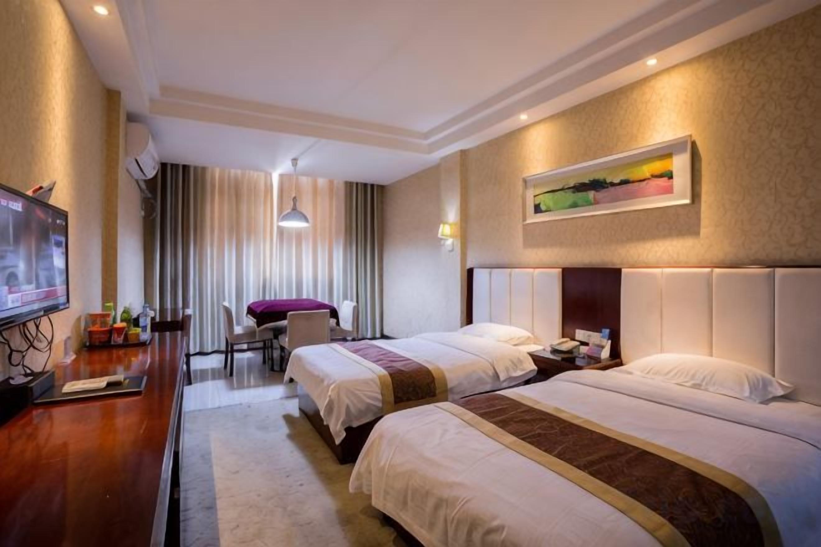 Habitación de hotel con dos camas, un escritorio con televisor, un área de comedor y un cuadro en la pared.
