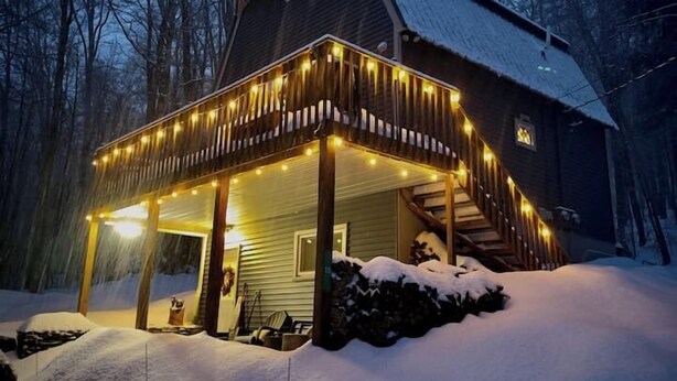 Une maison en bois avec un porche illuminé de guirlandes lumineuses, entourée de neige.
