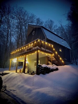 Ein Holzhaus mit Veranda, beleuchtet von Lichterketten, umgeben von Schnee.