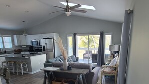 A spacious living area with a kitchen, a dining table with stools, a sofa, and a ceiling fan. - Private Murrells Inlet Waterfront 4 Bedroom 4 Bath Home on Marsh with Fire Pit (Murrells Inlet)