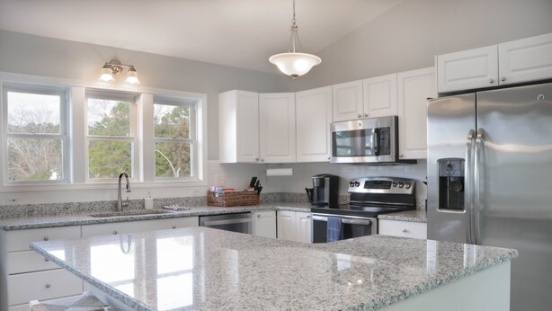 A modern kitchen with white cabinets, granite countertops, stainless steel appliances, and a large island with bar stools. - Private Murrells Inlet Waterfront 4 Bedroom 4 Bath Home on Marsh with Fire Pit (Murrells Inlet)