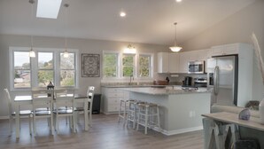 A modern kitchen with white cabinetry, a central island with stools, a microwave, and a refrigerator. - Private Murrells Inlet Waterfront 4 Bedroom 4 Bath Home on Marsh with Fire Pit (Murrells Inlet)