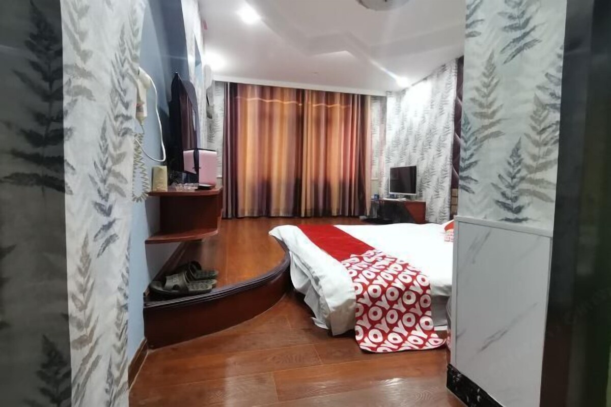 Una habitación de hotel con una cama, televisión, escritorio y una estantería con objetos.