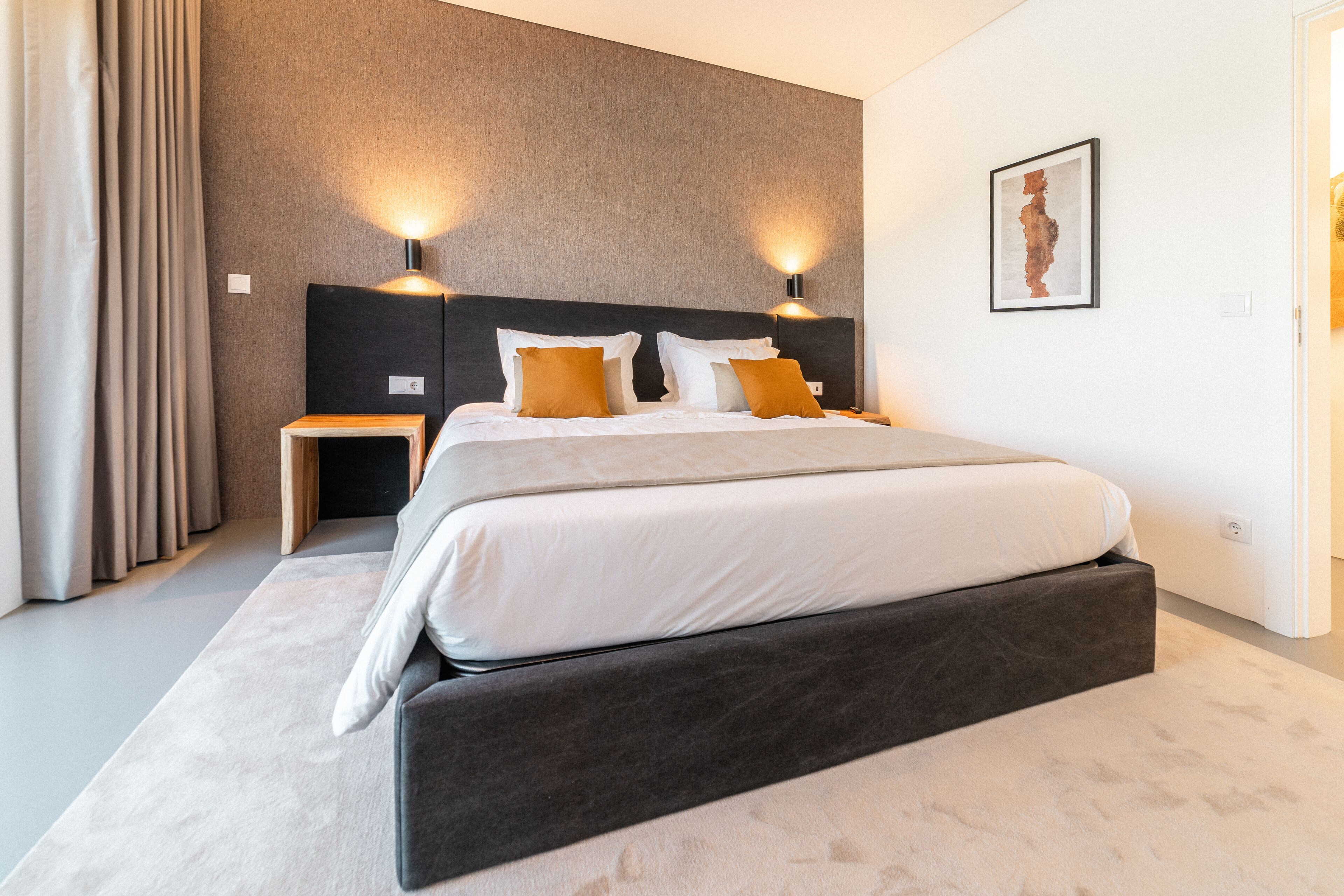 Une chambre d’hôtel moderne avec un grand lit, deux tables de chevet et une œuvre d’art accrochée au mur.