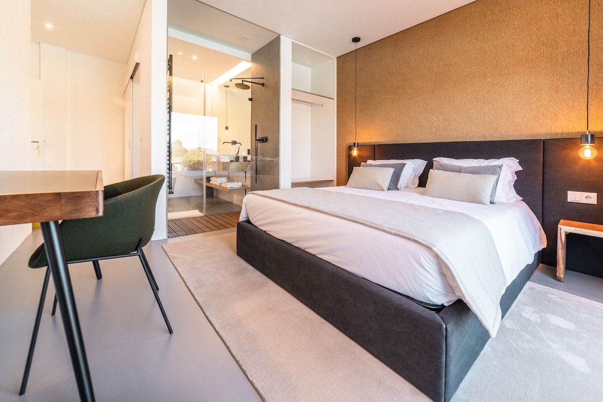 A modern hotel room with a large bed, a desk, and a shower area.