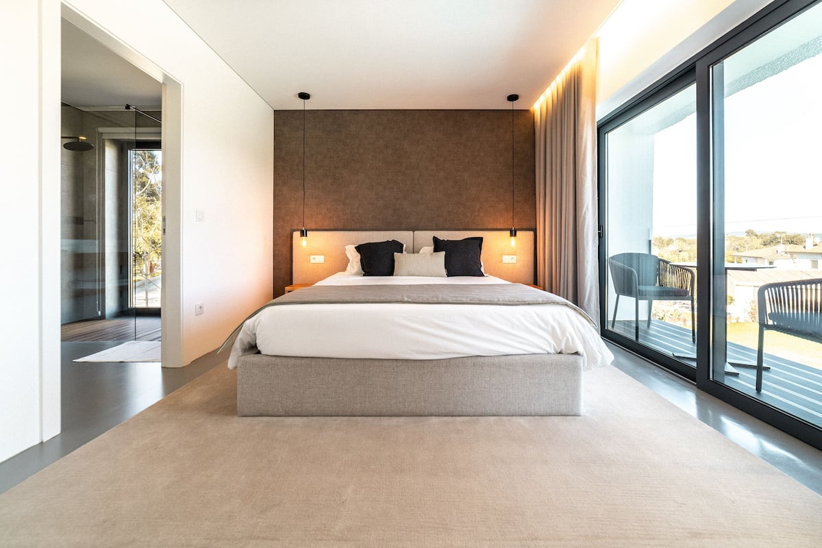 A modern bedroom with a large bed, a view of the outdoors through a sliding glass door, and a minimalist design.