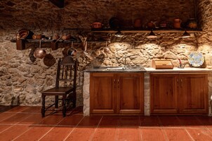 Una cocina rústica con paredes de piedra, armarios de madera y piso de baldosas.
