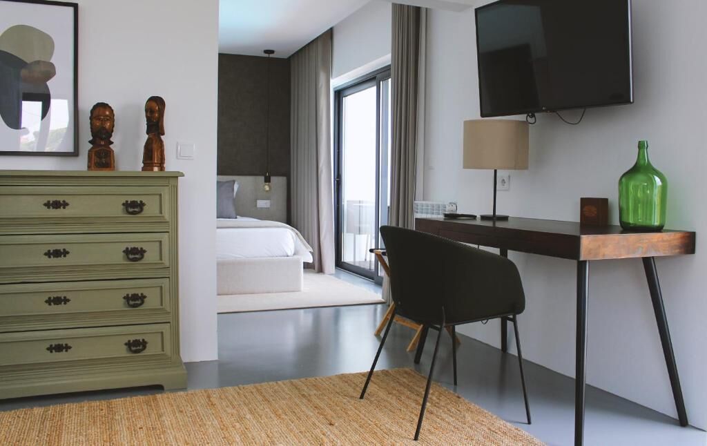 Une chambre d’hôtel moderne, équipée d’un lit, d’un bureau avec une lampe, d’une télévision et d’une bouteille verte posée sur le bureau.