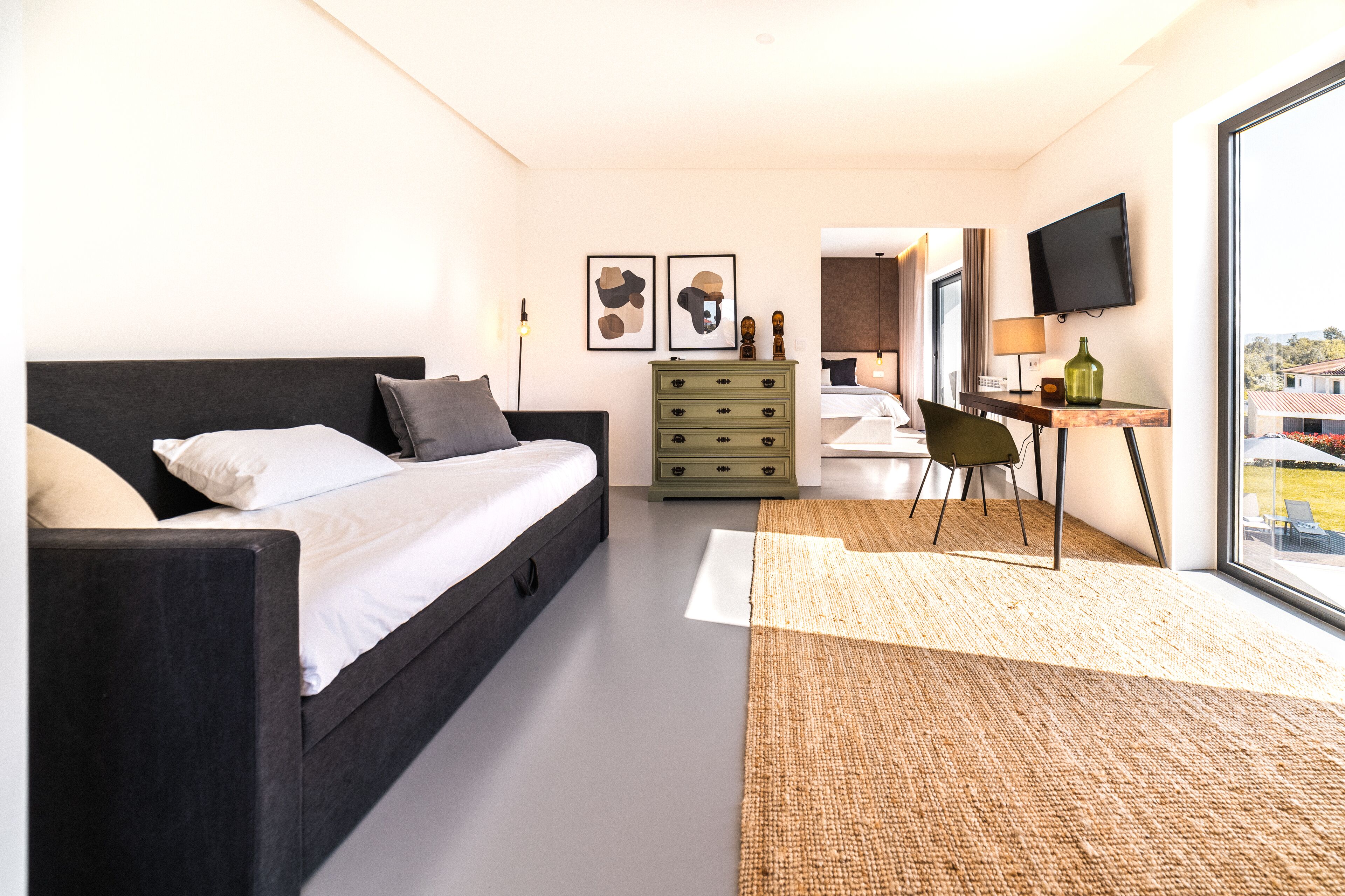 Una habitación de hotel moderna con cama, escritorio, silla, cómoda y televisor.