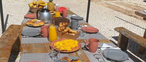 A picnic table set outdoors with various food items and drinks.