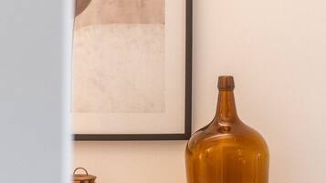 Un cuadro abstracto enmarcado en una pared, una botella marrón en un estante y una pequeña olla de cobre.