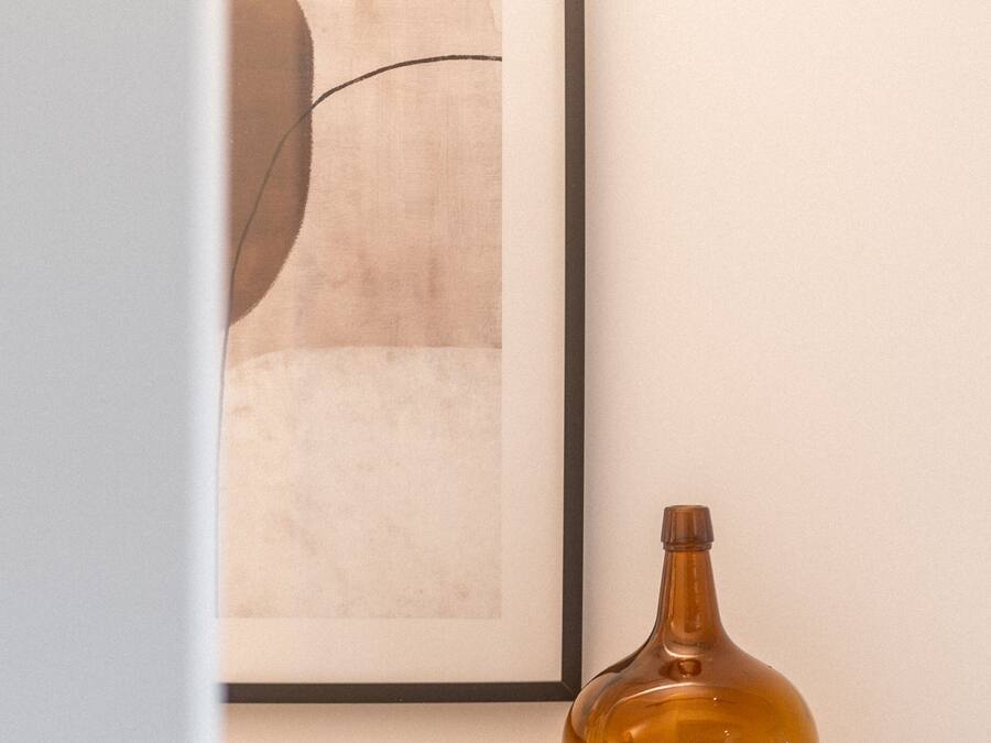 Un cuadro abstracto enmarcado en una pared, una botella marrón en un estante y una pequeña olla de cobre.