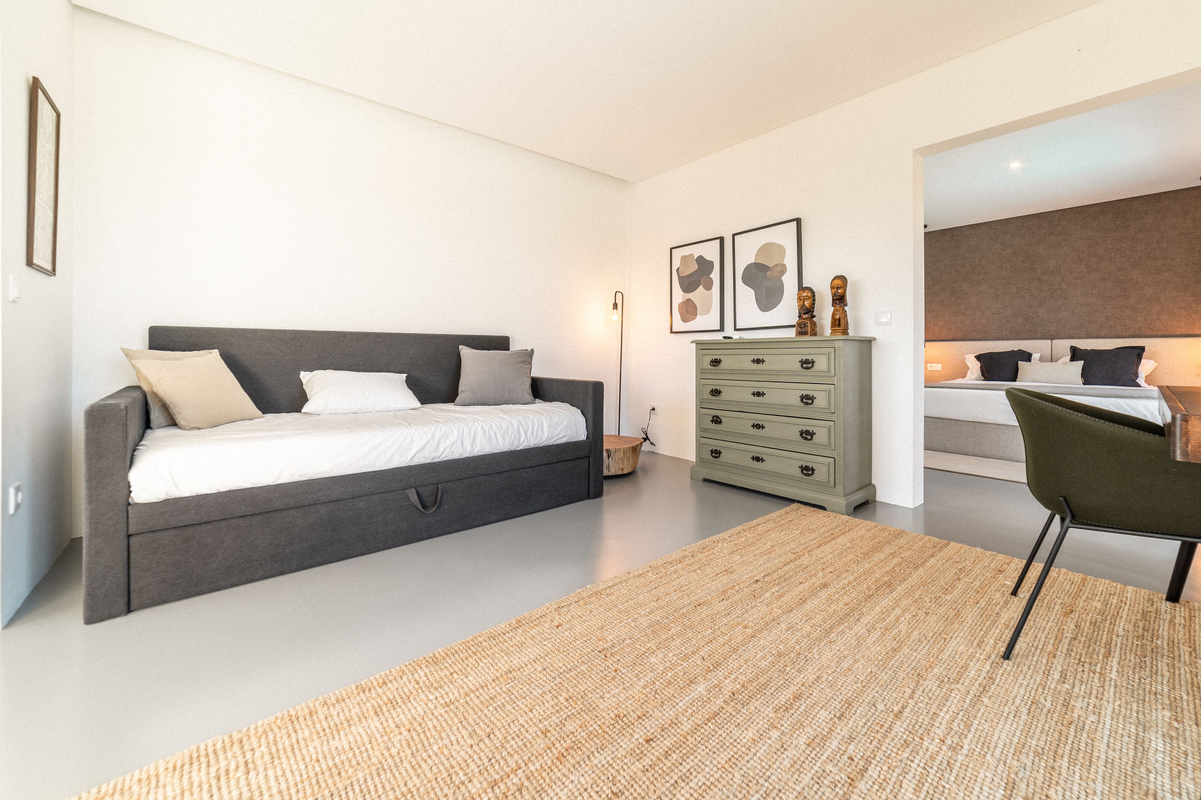 A modern bedroom with a grey sofa bed, a green dresser, and a green chair.