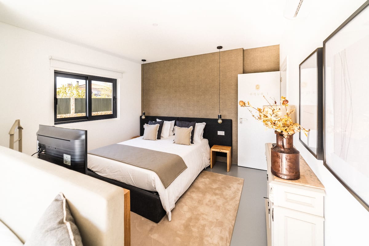 A modern bedroom with a bed, bedside tables, a dresser, and a window.