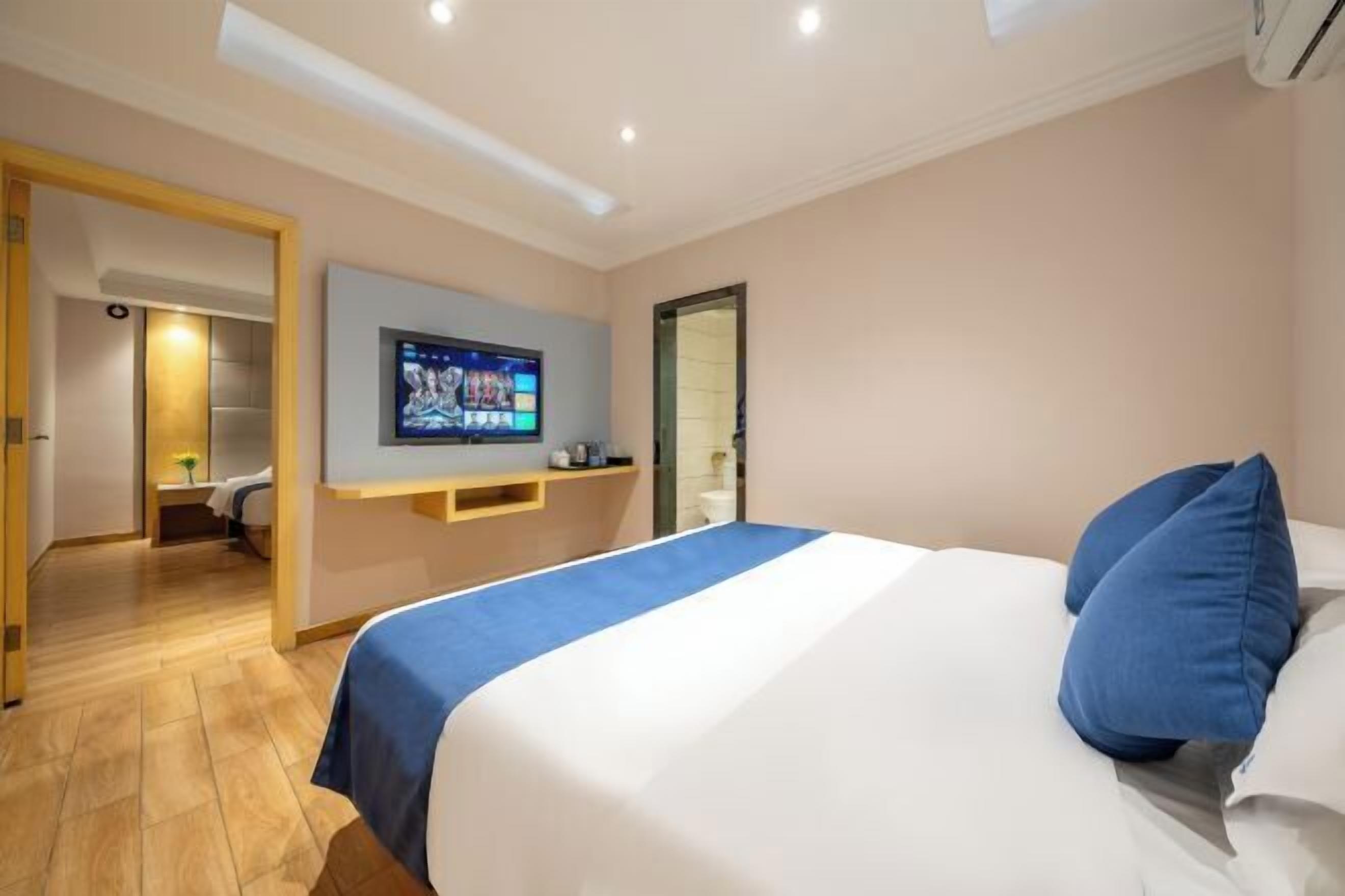 A hotel room with a bed, a TV mounted on the wall, and a wooden floor.