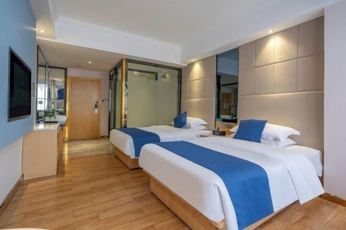 A hotel room with two beds, a TV, a desk, and a mirror.