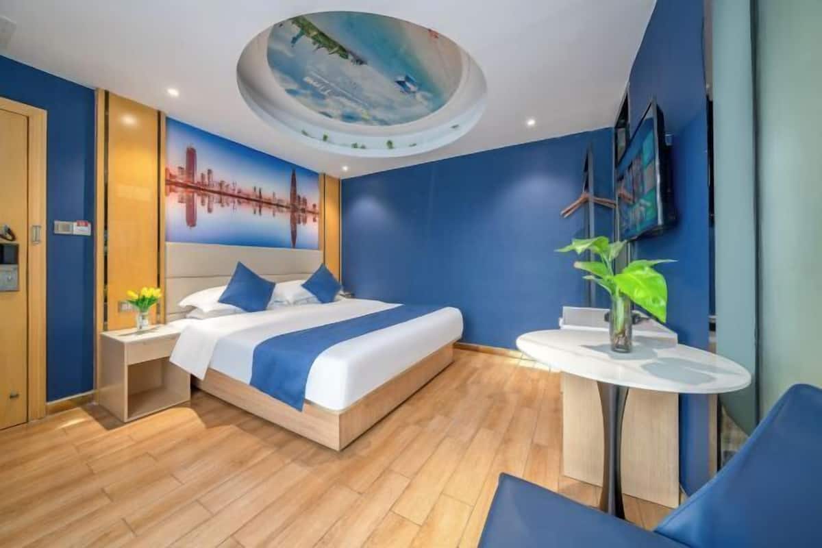 A modern hotel room with a large bed, a round ceiling feature, a cityscape mural, and a small table with a plant.