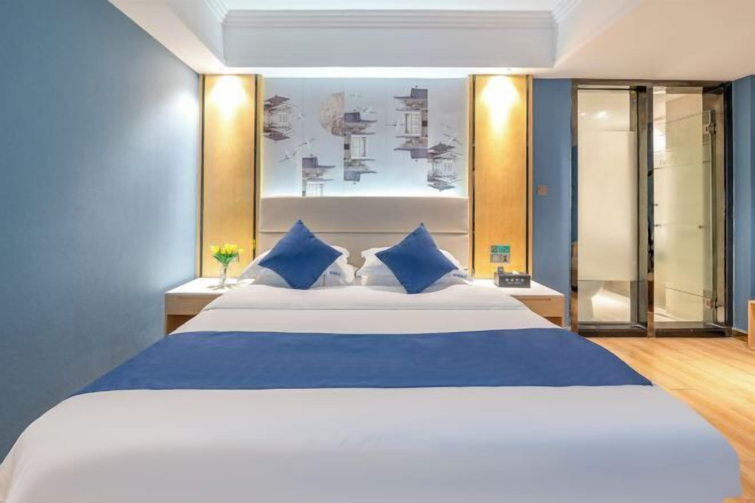 Ein modernes Hotelzimmer mit einem großen Bett, zwei Nachttischen, einem Wandbild und einer Schiebetür zum Badezimmer.