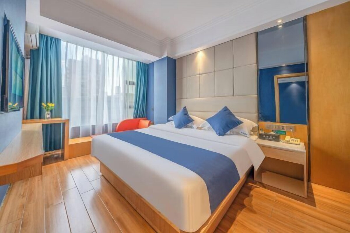 A hotel room with a large bed, a bedside table, a desk, and a window with curtains.