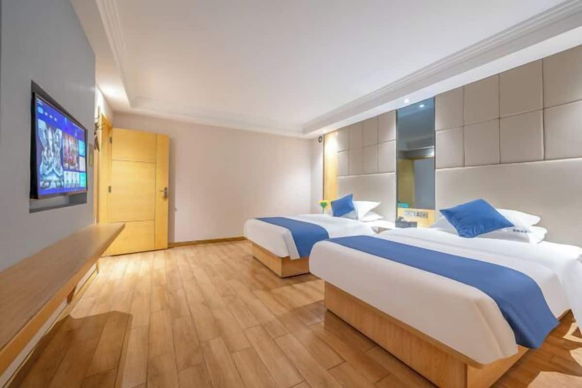 A hotel room with two beds, a wooden floor, a television, and a large padded headboard.