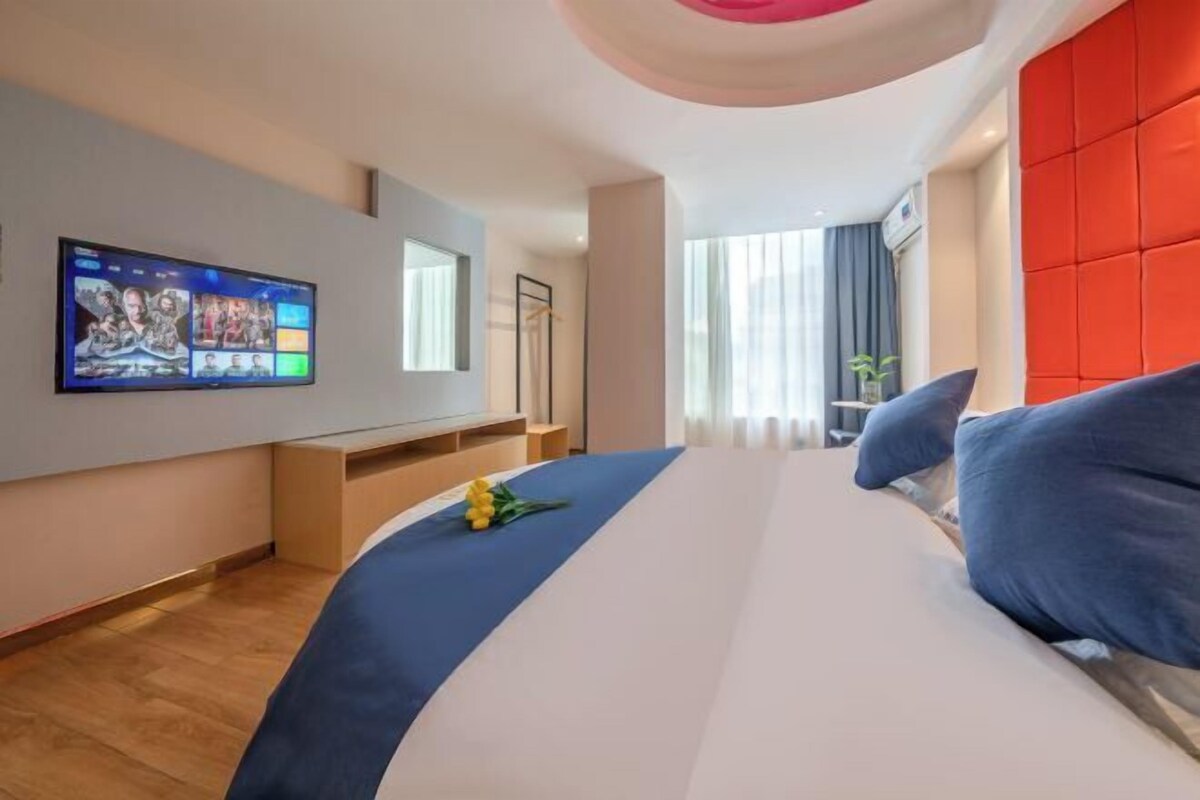 A modern hotel room with a large bed, a flat-screen TV mounted on the wall, and a bright red accent wall.