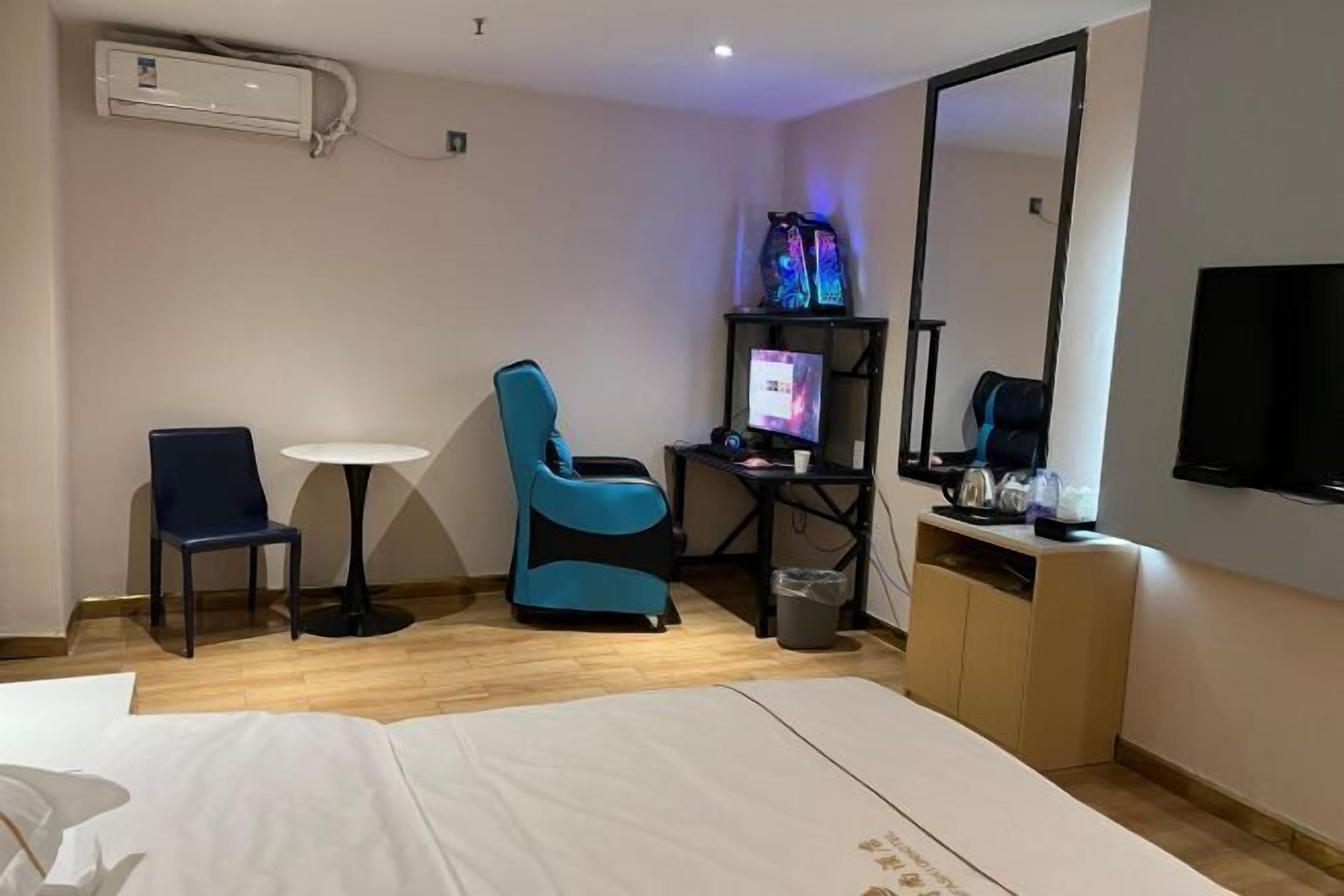 A hotel room with a bed, a desk with a computer, a chair, a small table, and a TV.