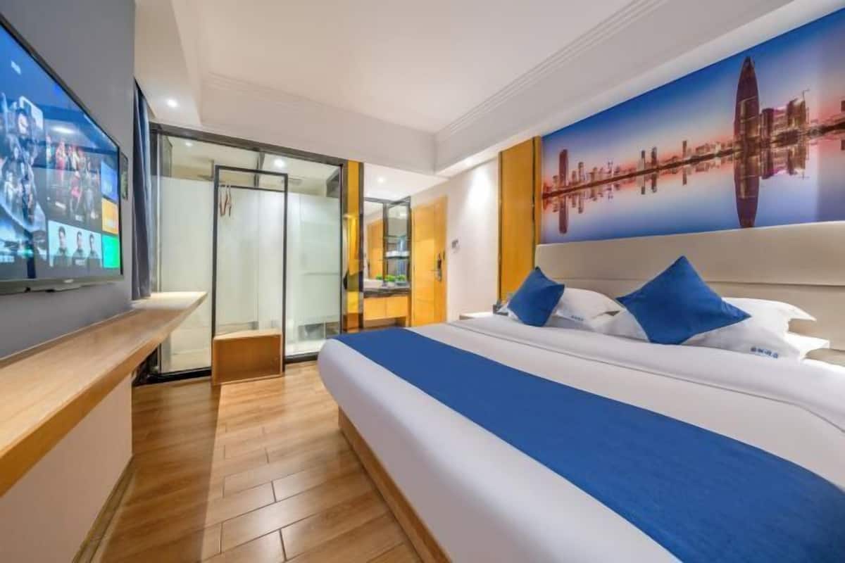 A hotel room with a large bed, a TV on the left, and a cityscape mural on the wall.
