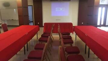 Un salón de conferencias con una larga mesa, sillas rojas y una pantalla para proyector.