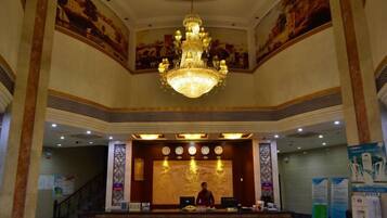 A lobby with a grand chandelier, a reception desk, and a staircase leading to upper floors.