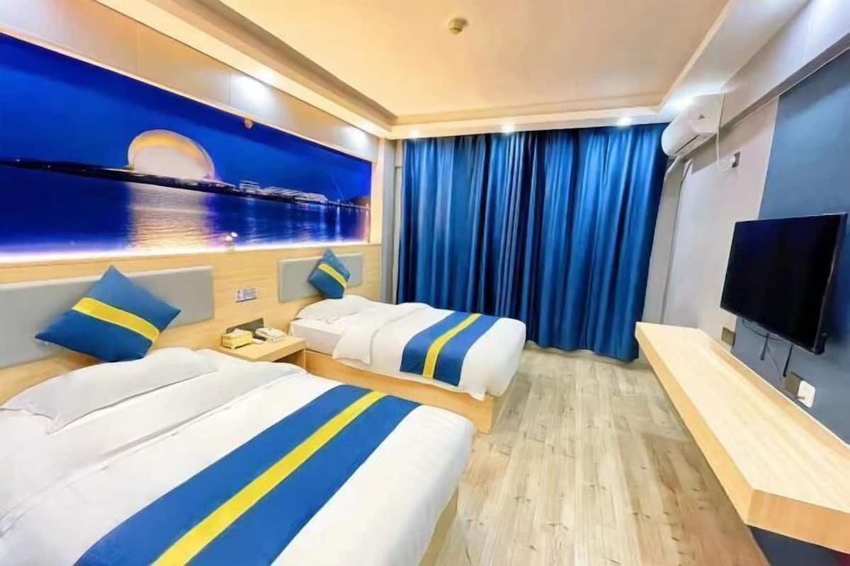 Habitación de hotel con dos camas, televisión, escritorio y un ventanal grande con cortinas.