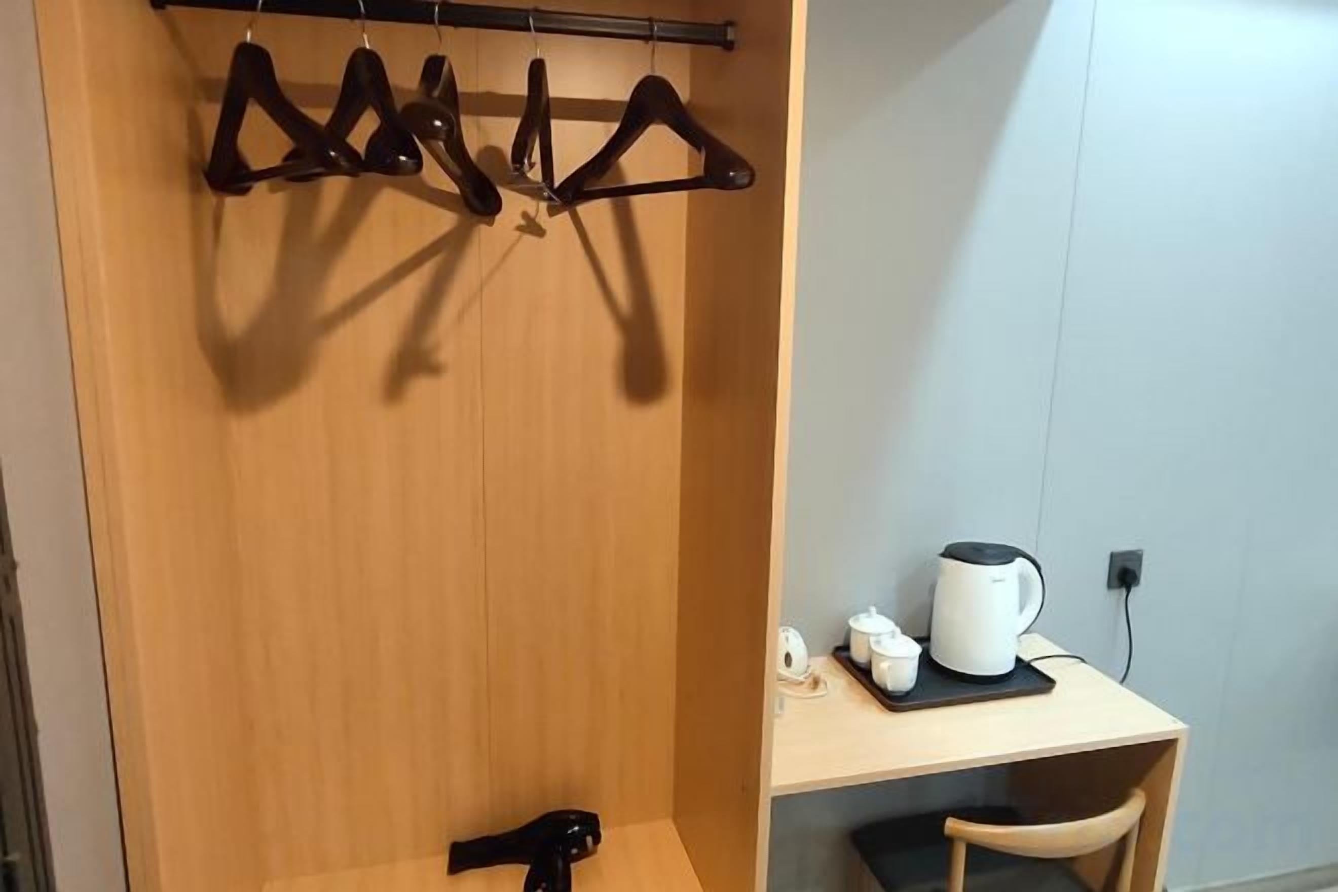 A wooden wardrobe with a coat rack, a small table with a white mug and a black object, and a chair.
