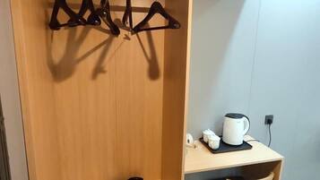 A wooden wardrobe with a coat rack, a small table with a white mug and a black object, and a chair.