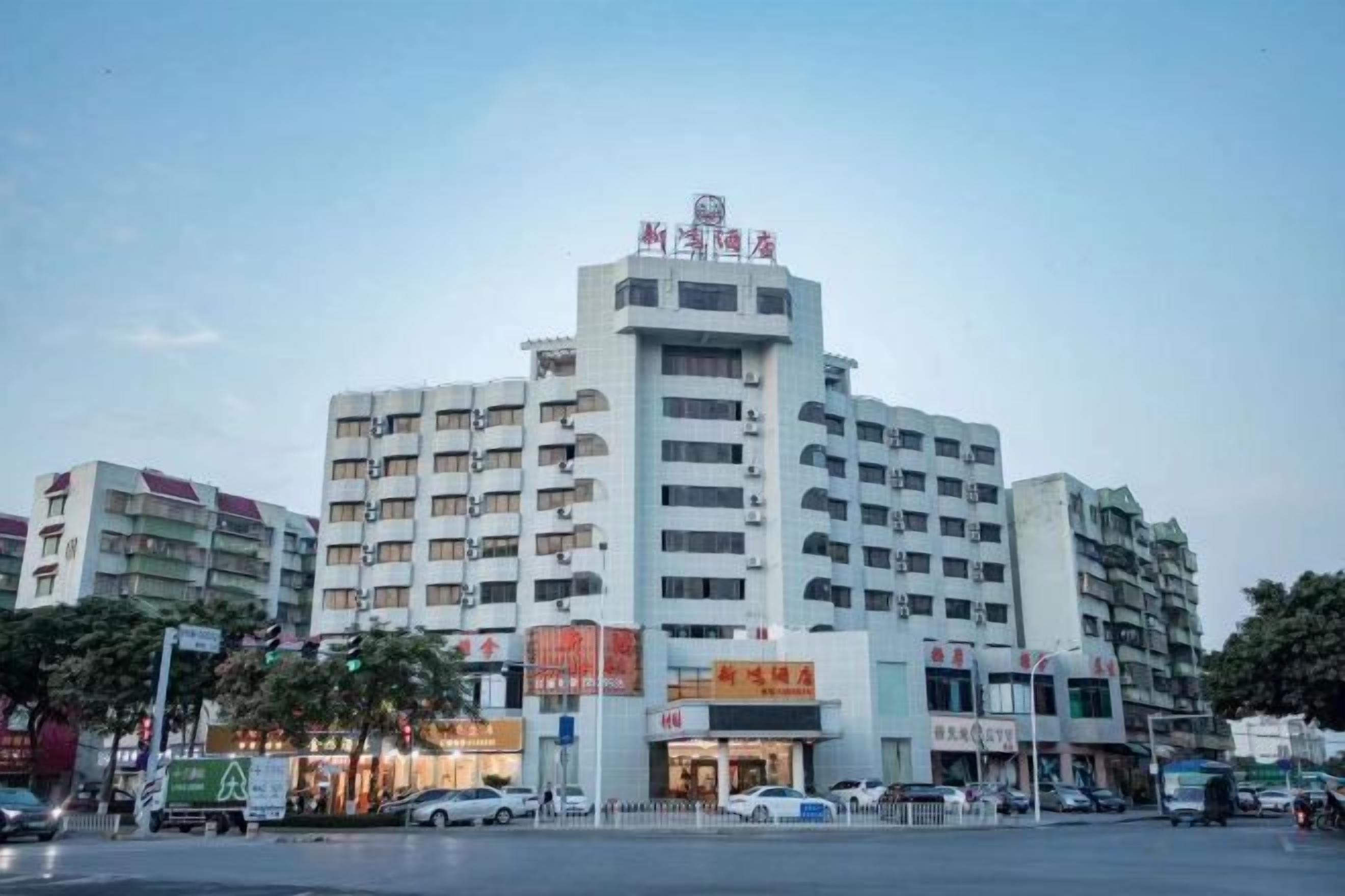 Ein mehrstöckiges Hotel mit einer auffälligen Schilderung oben, mehreren Etagen und einer Straßenszene mit Autos und Fußgängern.