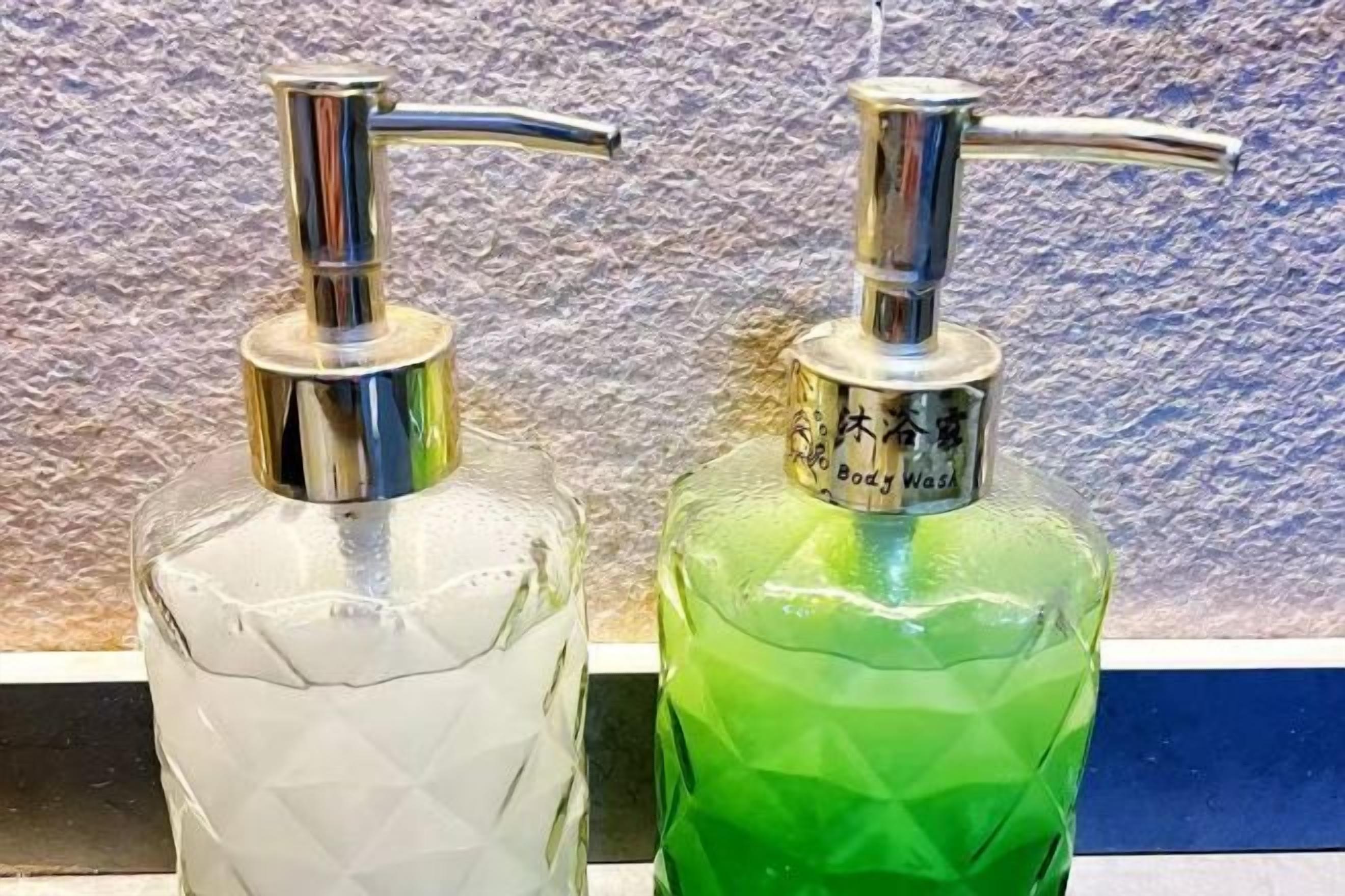 Deux distributeurs de savon liquide pour les mains, l’un transparent et l’autre vert, avec des pompes métalliques.