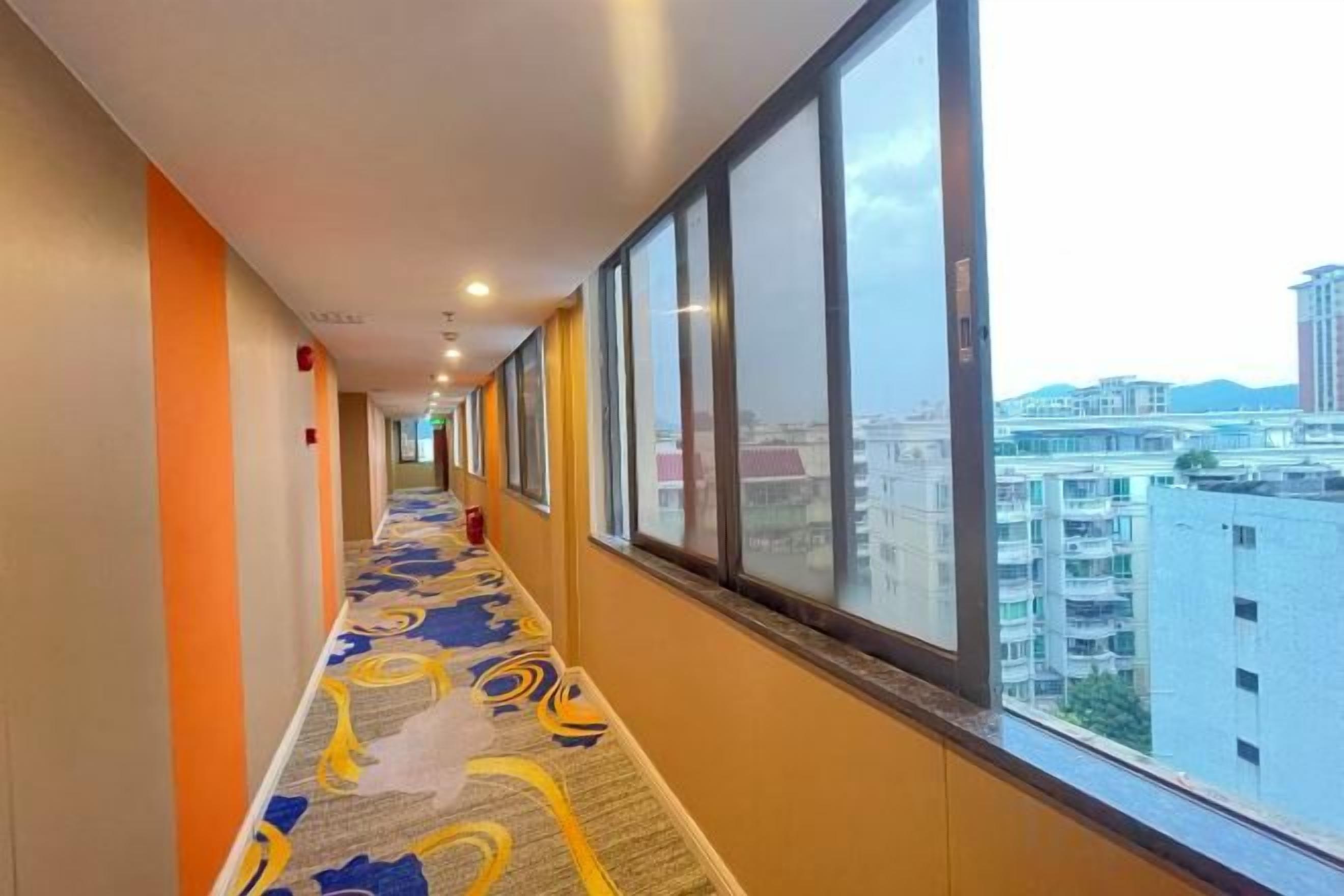 A hotel corridor with a patterned carpet, large windows, and a view of buildings.