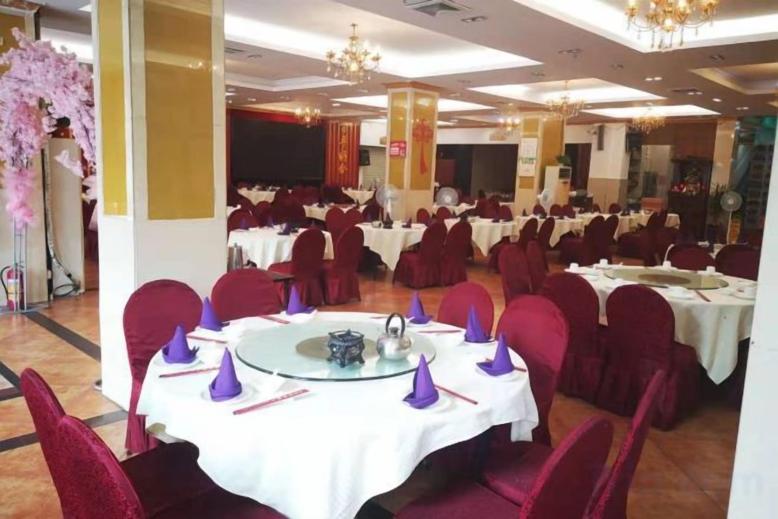 A banquet hall with round tables, red chairs, and a stage in the background.