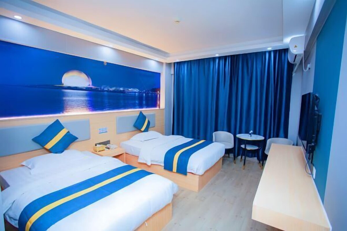 Habitación de hotel con dos camas, un escritorio, una silla y vista al mar.