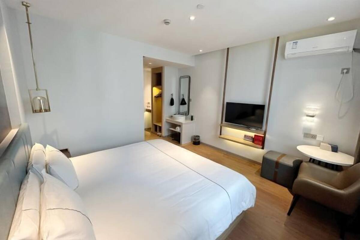 A hotel room with a bed, a TV, a desk, a chair, and a bathroom with a shower.