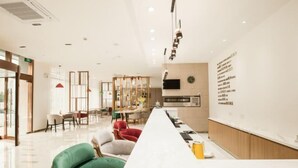 Un hall d'hotel modern amb una llarga recepció, zona de seients amb cadires i una cuina al fons.