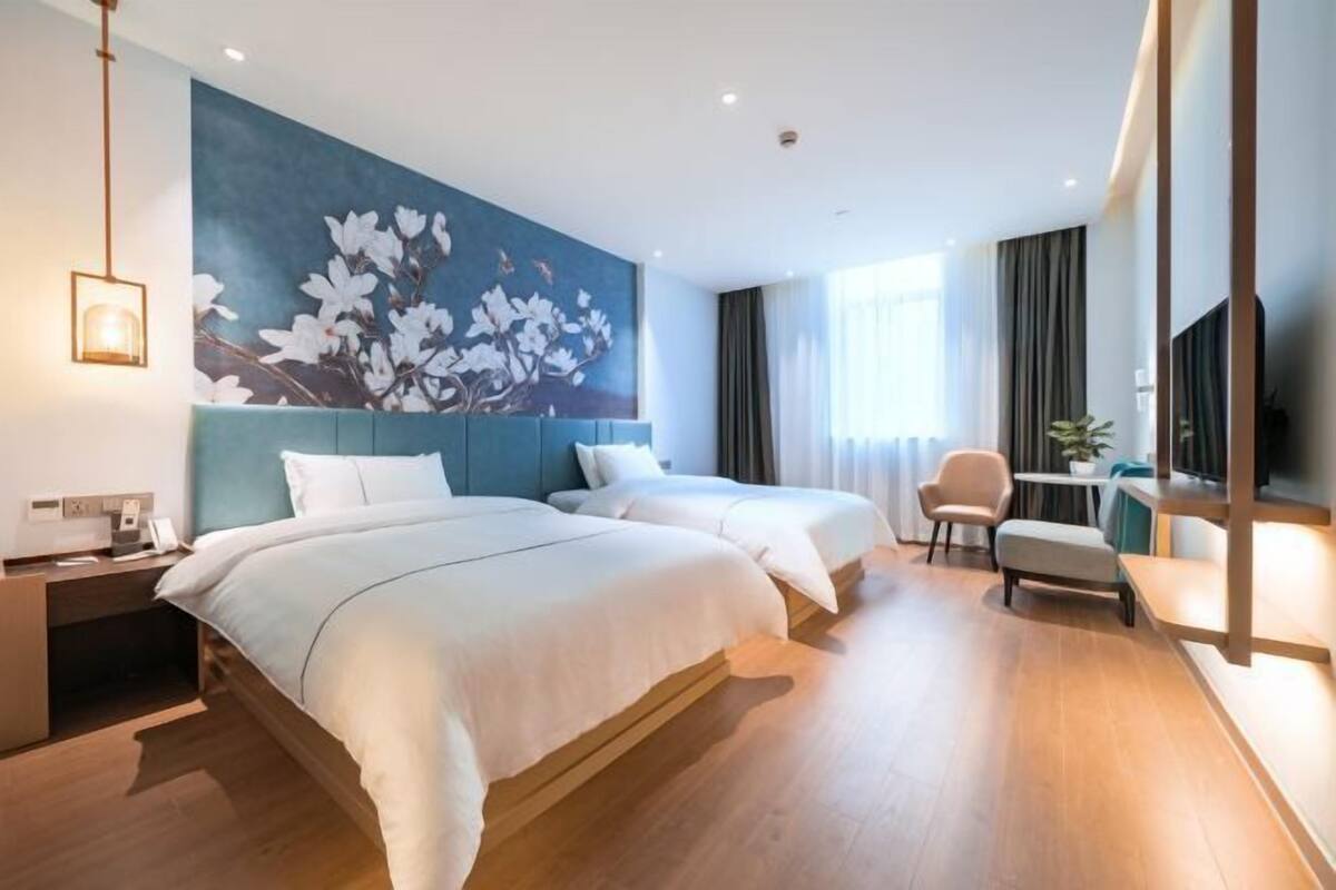 A hotel room with two beds, a desk, a chair, a TV, and a large floral mural on the wall.