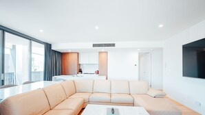 Una sala de estar moderna con un sofá seccional color beige, una mesa de centro blanca y una cocina al fondo.