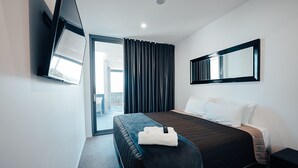 Una habitación de hotel moderna con una cama grande, un televisor de pantalla plana montado en la pared y una puerta corrediza de vidrio que da a un balcón.