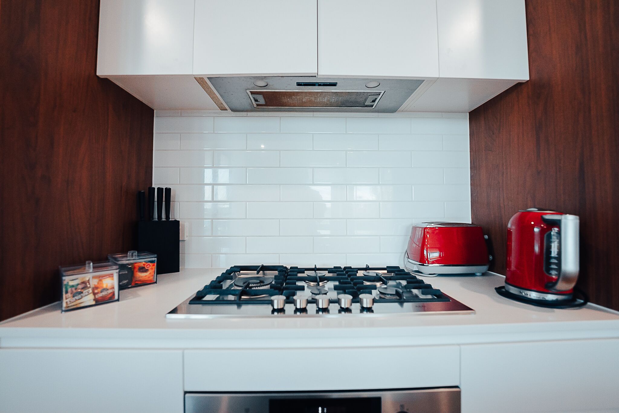 A kitchen with white cabinets, a gas stove, a red toaster, and a kettle.