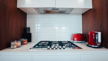 A kitchen with white cabinets, a gas stove, a red toaster, and a kettle.