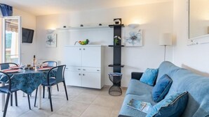 Un espacio habitable compacto con comedor, un sofá, un armario blanco y un televisor montado en la pared.