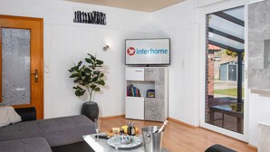 Ein modernes Wohnzimmer mit einem grauen Sofa, einem kleinen Tisch mit einem Getränk und einer Schale, einer Topfpflanze und einem Bücherregal.